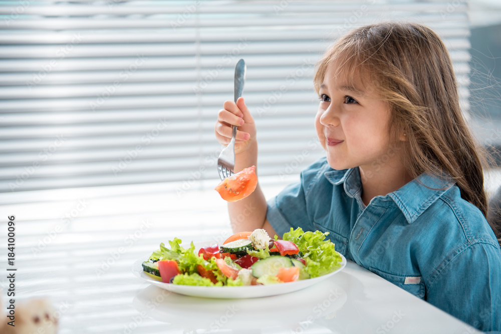 Side view profile of cute female child dreaming while eating salad in kitchen. Copy space Side view profile of cute female child dreaming while eating salad in kitchen. Copy space