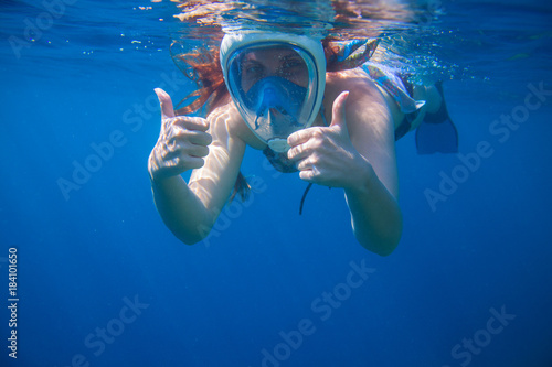 Girl underwater showing thumbs. Snorkeling woman in full face mask.