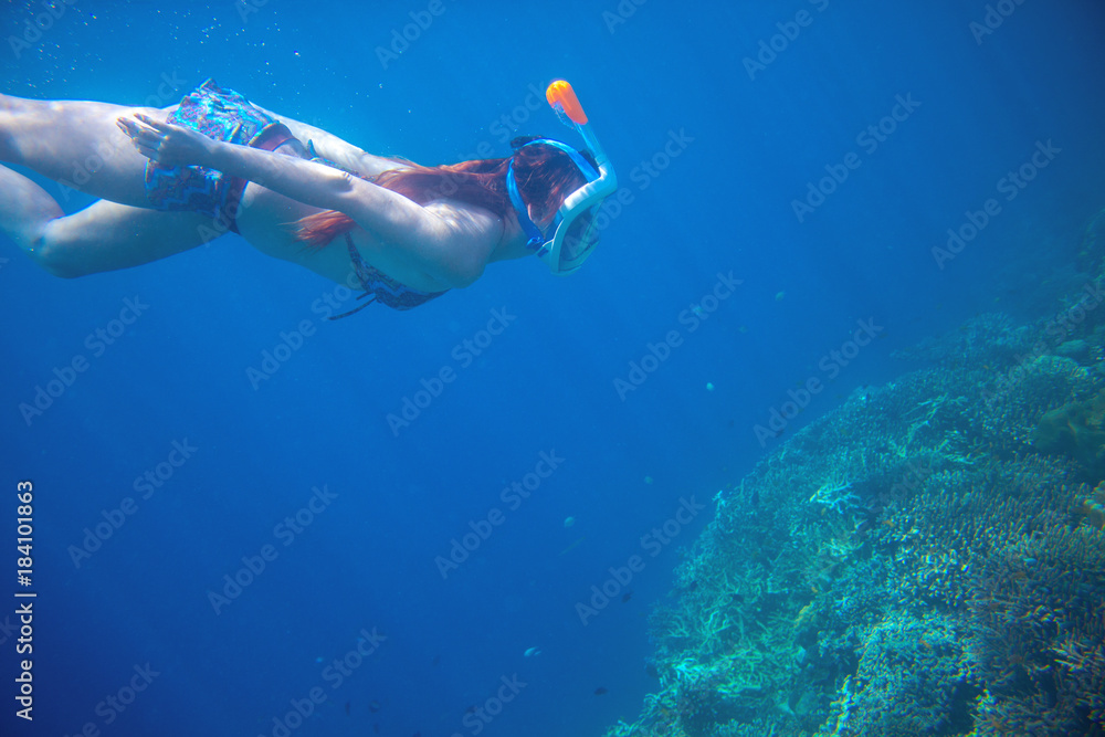 Diving girl underwater with coral reef. Snorkel in full face mask.