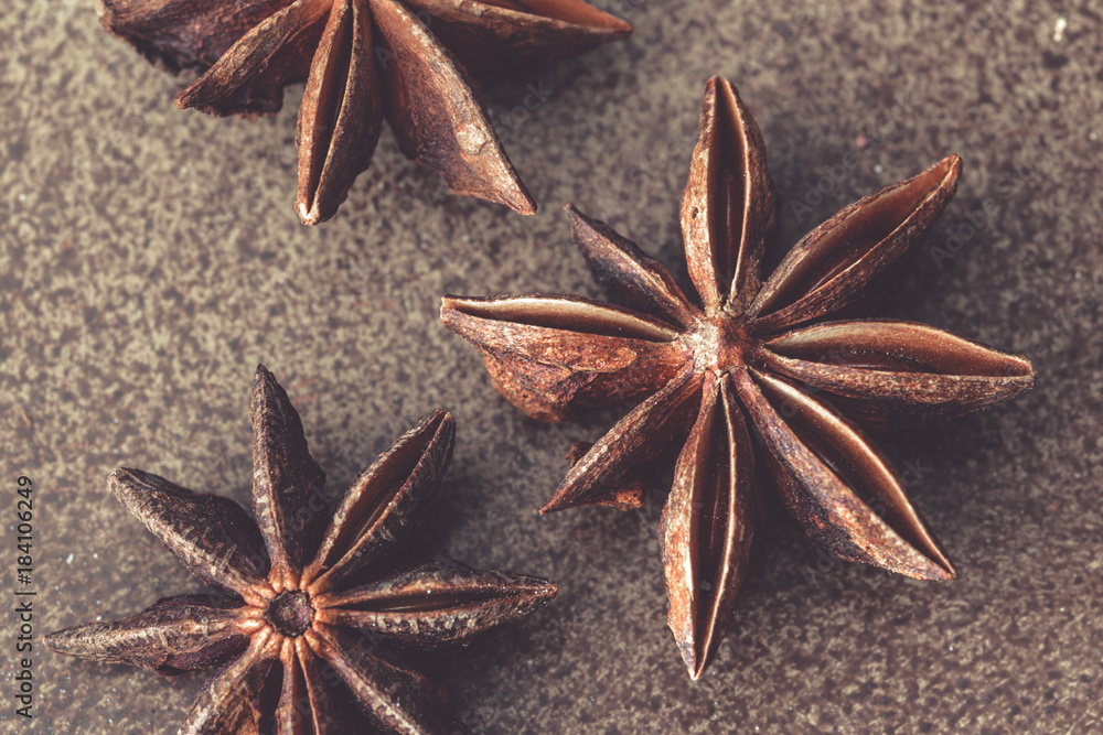 Three anise stars close up on a brown background.
