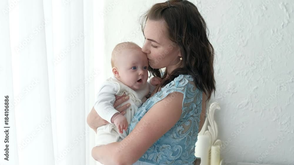 Tracking mother putting baby to sleep while walking . Attractive woman holding baby in hands and walk across living room with bright window curtains in background. Tracking mother putting baby to sleep while walking . Attractive woman holding baby in hands and walk across living room with bright window curtains in background.