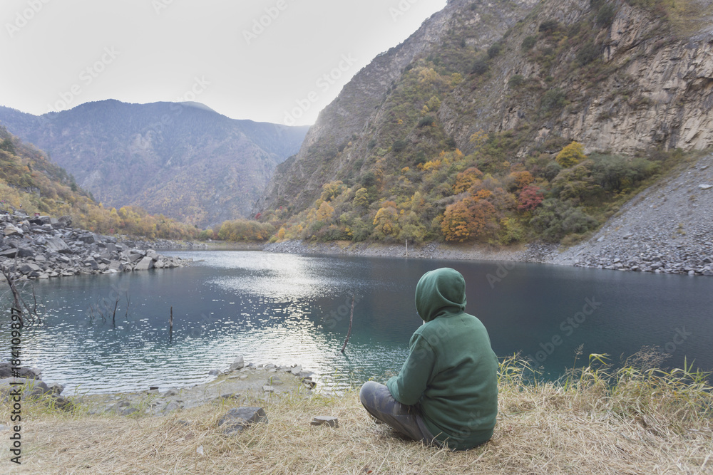 A man in a green jacket sits by the lake