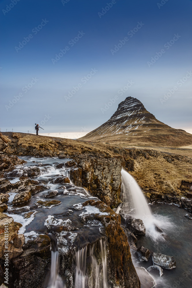 A photographer stands in front of the amazing landscape of Kirkjufell in the west of Iceland, Europe.
