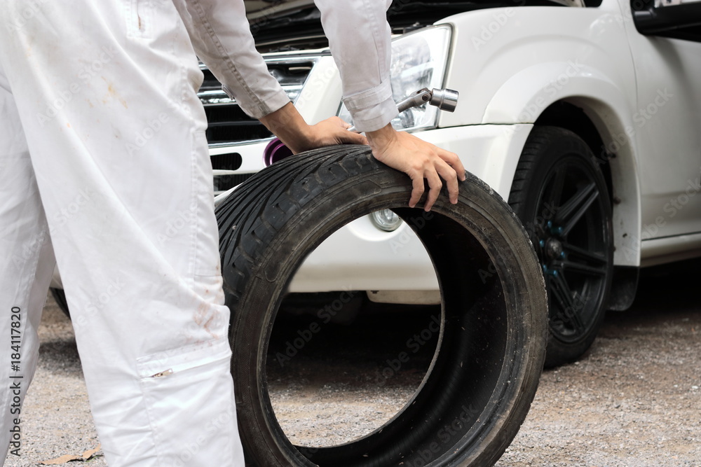 Fototapeta premium Selective focus on hands of professional mechanic in uniform holding wrench and tire at the repair garage background. Insurance car concept.