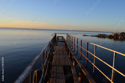 The old pier in the Volga River, lit by the sun at sunset, surrounded by water and clear sky © Ilia