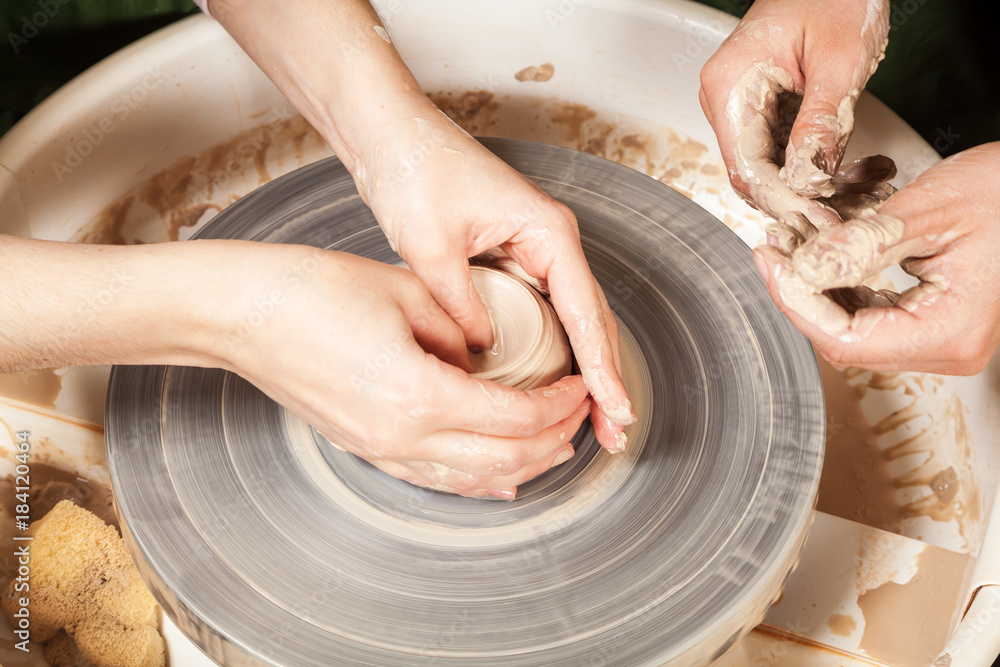 Close-up of a woman potter teaches a student sculpts from a brown clay on a potter's wheel a deep cup in a workshop