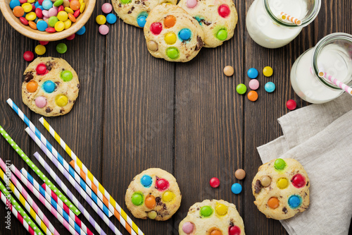 Children's cookies with colorful chocolate sweets in sugar glaze on a brown wooden background. Selective focus. Top view. Place for text.