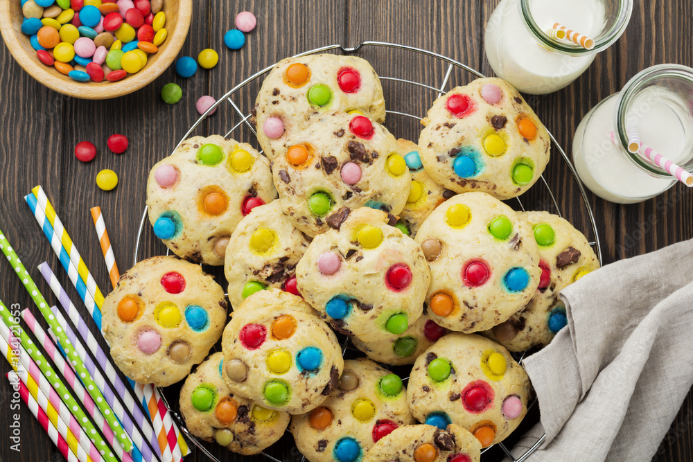 Children's cookies with colorful chocolate sweets in sugar glaze on a brown wooden background. Selective focus. Top view. Place for text.