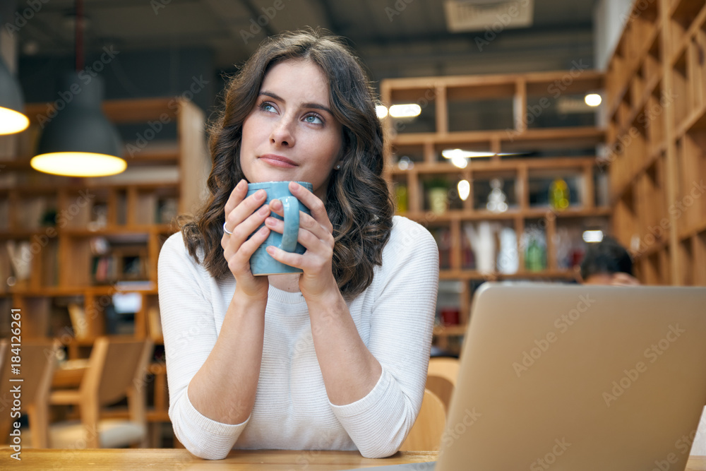 Beautiful young woman girl holding mug in front of her with two hands and a  wistful dreamy expression looking up sitting at a table in a cafe with  laptop Photos | Adobe