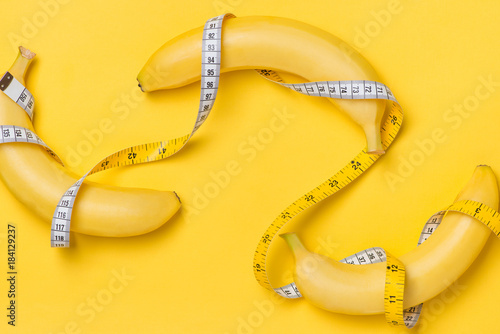 Diet, fitness and health concept presented by yellow banana wrapped in measure tape isolated on yellow paper background