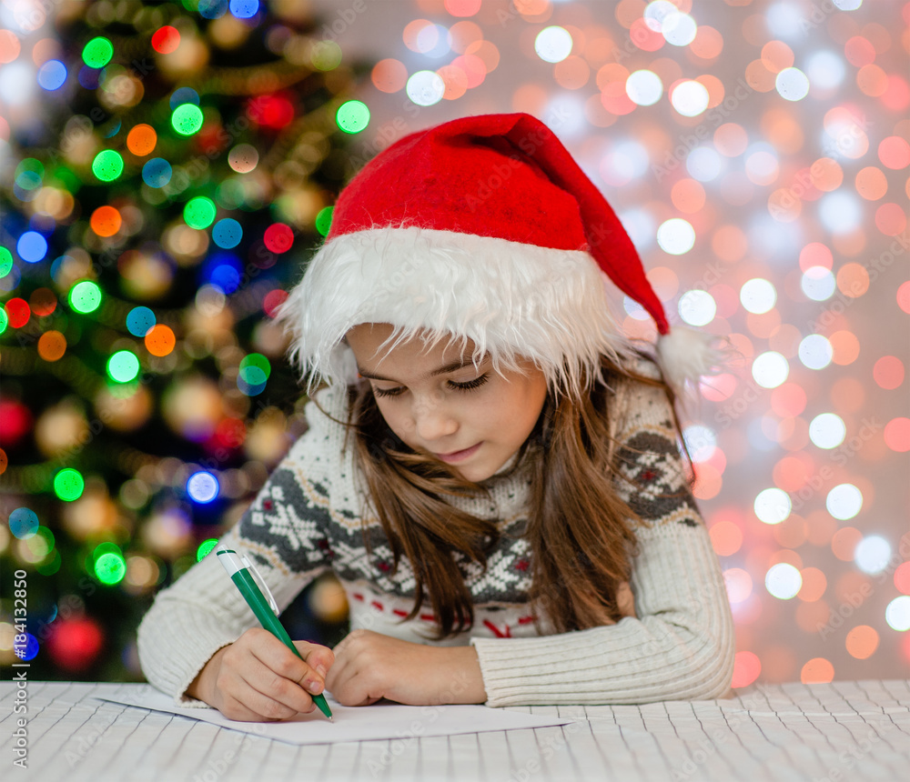 Happy little girl in red christmas hat writes letter to Santa Claus Happy little girl in red christmas hat writes letter to Santa Claus