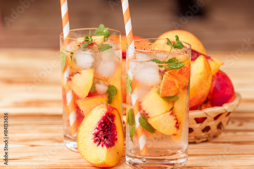 Peach lemonade with ice and mint leaves. Homemade lemonade of ripe nectarine with white and orange ripe. Two glasses of peach tea. Refreshing summer drink on a white wooden background.