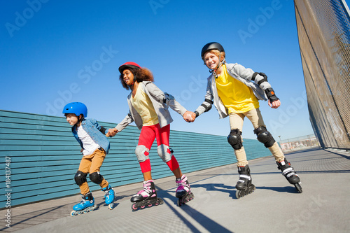 Kids holding hands while rollerblading outdoors