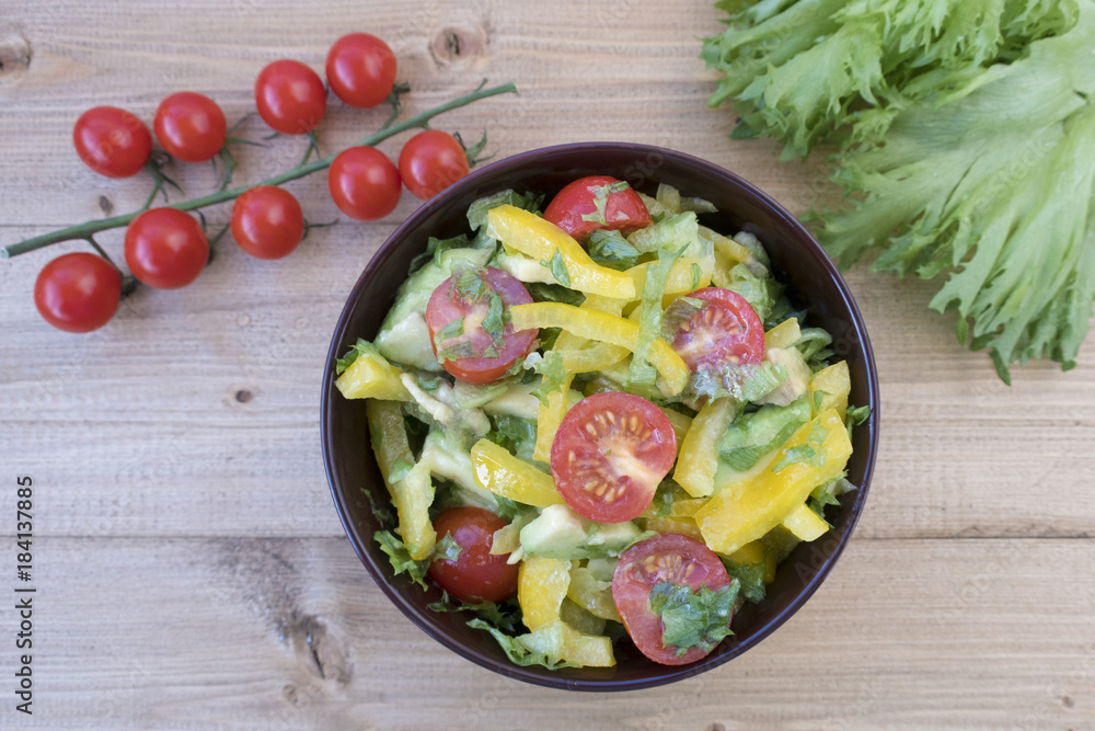 Appetizing vegetable salad consisting of tomatoes, avocado, yellow sweet pepper, lettuce and seasonings.
