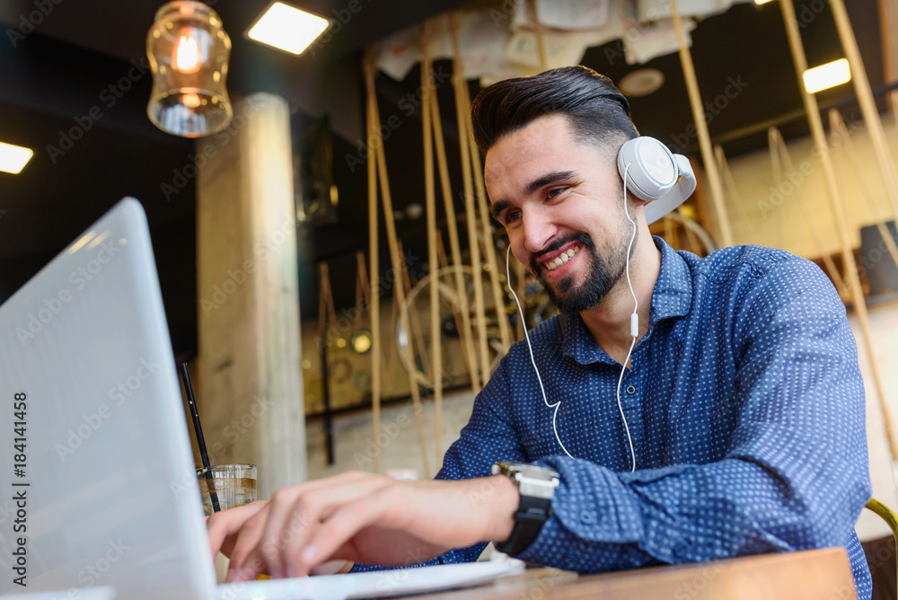 Cheerful Young Man Using Tablet with Earphones In Coffee Shop Listening Music