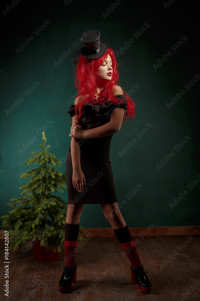 portrait of a teenage girl in a black dress with a red wig and in a carnival hat. Christmas new year