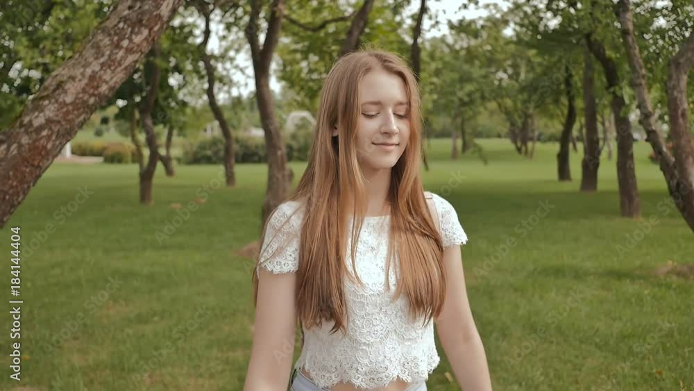 A young girl is engaged in a walk in the park, looking at a smart clock on her arm and receiving a pulse measurement. Health. Sport. Recreation. Summer. A young girl is engaged in a walk in the park, looking at a smart clock on her arm and receiving a pulse measurement. Health. Sport. Recreation. Summer.