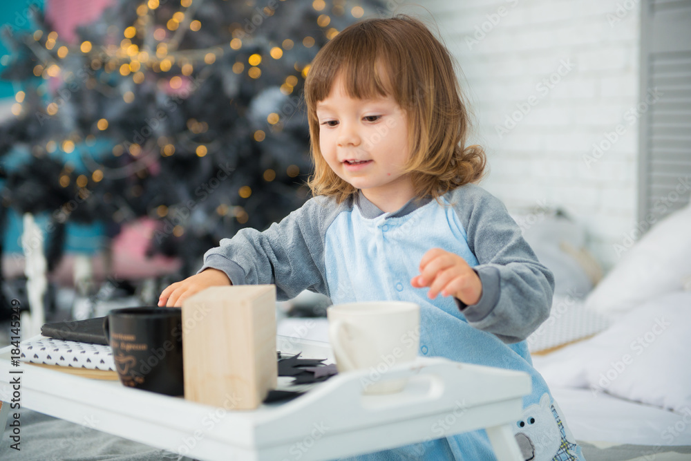 Emotional smiling little girl sitting in pajama with Christmas gifts near New Year's tree and playing snowballs Emotional smiling little girl sitting in pajama with Christmas gifts near New Year's tree and playing snowballs