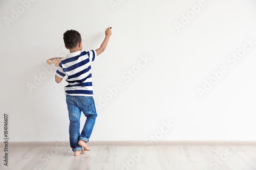 Fototapeta Naklejka Na Ścianę i Meble -  Little African-American boy painting on wall indoors