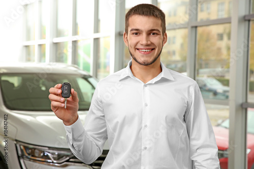Handsome car salesman holding key in dealership centre