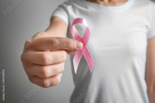 Woman holding pink ribbon on grey background. Breast cancer awareness concept