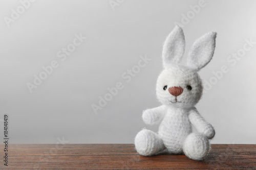 Cute knitted bunny toy on table against light background