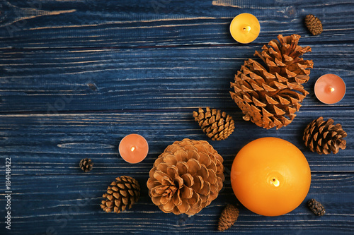 Composition with burning candles and pine cones on wooden background, top view