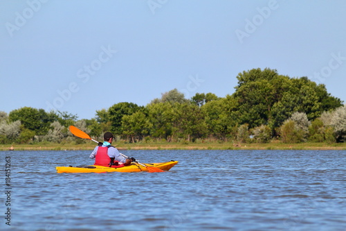 Man in yellow kayak paddling at river on biosphere reserve in spring. Kayaking in Danube river. Concept for adventure, travel, action, lifestyle