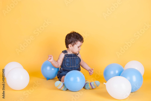 toddler in denim overalls with inflatable balls on a bright yellow background