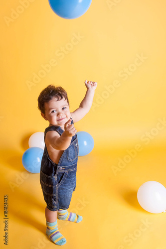 toddler in denim overalls with inflatable balls on a bright yellow background