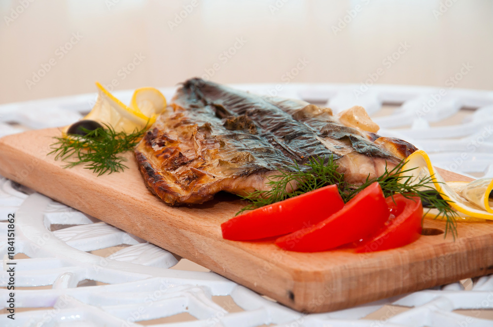 Grilled fish on a wooden board with lemon and tomatoes Grilled fish on a wooden board with lemon and tomatoes