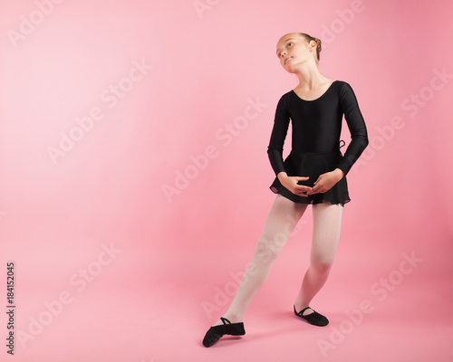 Portrait of young beautiful child girl ballerina standing practicing ballet wearing black tutu dress posing in studio with light pink background.