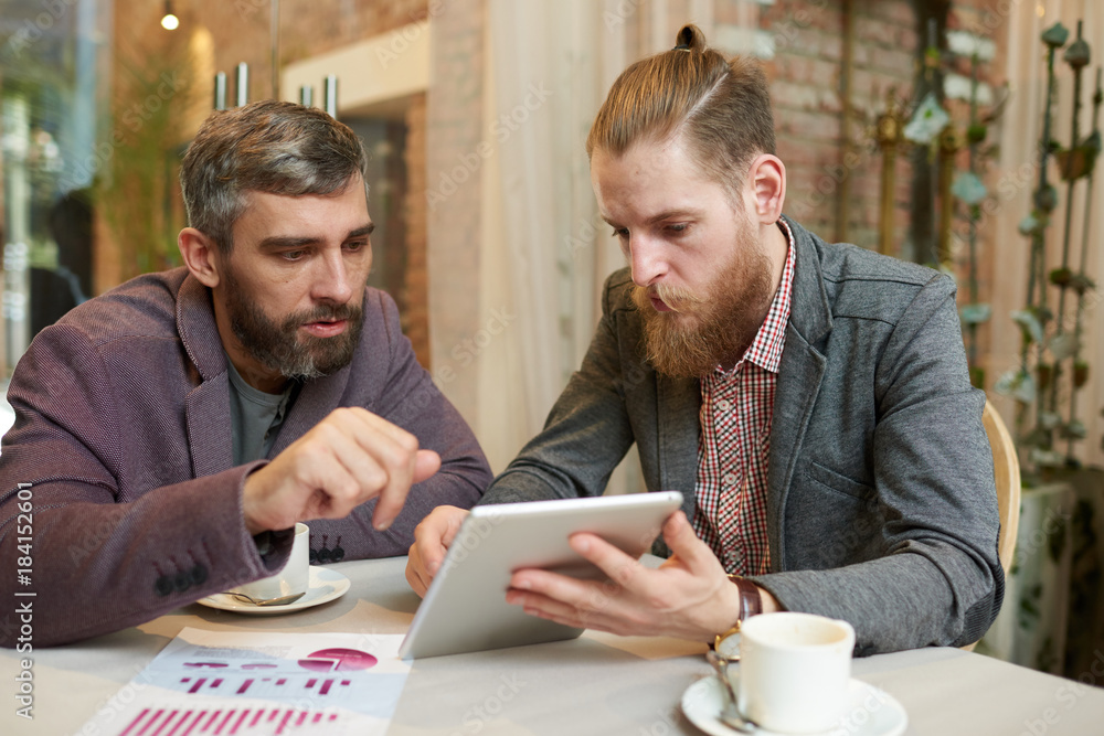Portrait of two modern business people discussing work and using digital tablet during meeting in cafe on coffee break Portrait of two modern business people discussing work and using digital tablet during meeting in cafe on coffee break