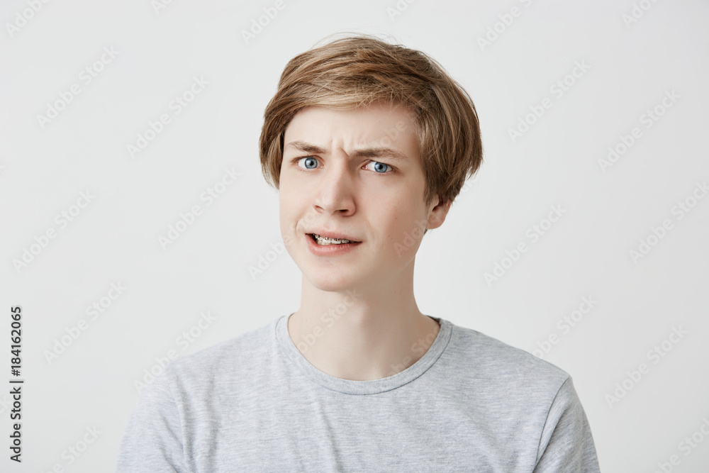 Grumpy irritated fair-haired young male being emotional and angry after offended by cruel man, recieves bad words, isolated against gray background. Bewilderment concept Grumpy irritated fair-haired young male being emotional and angry after offended by cruel man, recieves bad words, isolated against gray background. Bewilderment concept