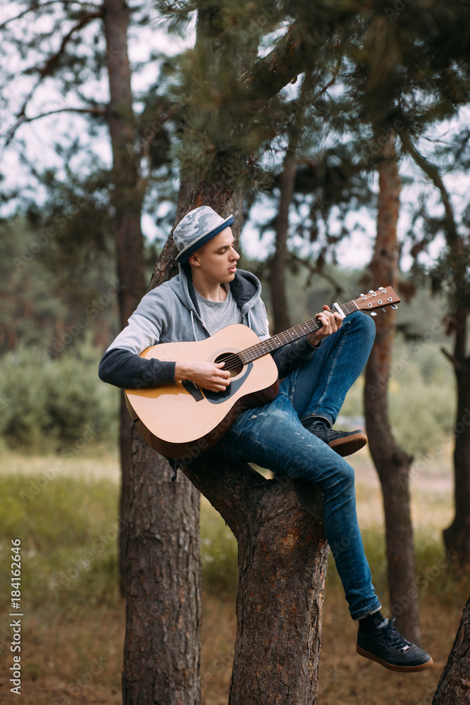 Handsome boy playing guitar tree forest concept. Unity with nature. Hiking happy moments. Handsome boy playing guitar tree forest concept. Unity with nature. Hiking happy moments.