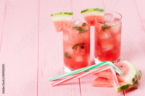 Watermelon lemonade with ice and mint leaves. Homemade lemonade of ripe berry with red and green ripes. Glass of cold watermelon tea. Refreshing summer drink. Cocktail on a wooden background