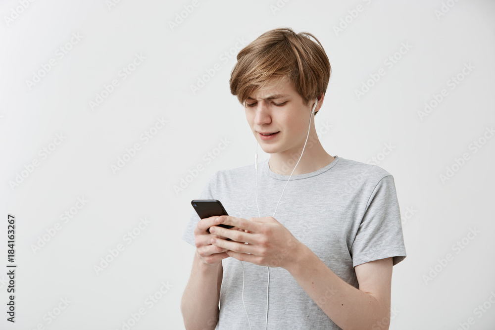 Shocked puzzled hipster guy messages with friends, uses free internet connection on modern cell phone, receives bad news. Astonished young male recieves bad news. Human feelings, emotions, reaction Shocked puzzled hipster guy messages with friends, uses free internet connection on modern cell phone, receives bad news. Astonished young male recieves bad news. Human feelings, emotions, reaction