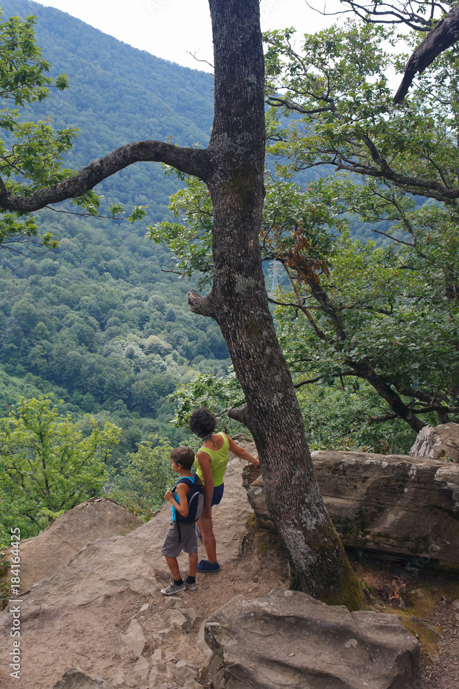 Naklejka premium Mom and little son tourists are looking from the high mountain to the view below