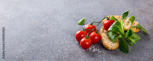 Gray stone background with cherry tomatoes, wholewheat rusks and corn salad. Healthy food concept with copy space. Banner