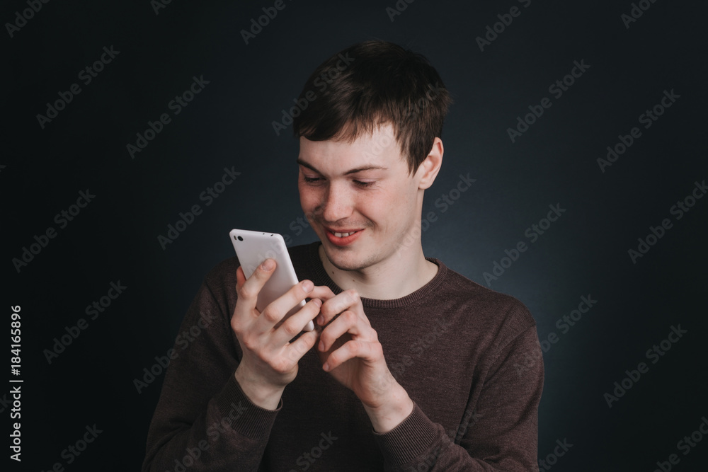 A man looks at a mobile phone screen and dials the message , the portrait of a man close up in Studio on dark background A man looks at a mobile phone screen and dials the message , the portrait of a man close up in Studio on dark background