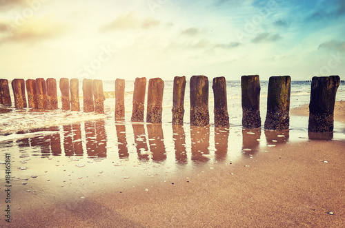 Vintage toned picture of an old wooden breakwater on a beach at sunset, nature background. 