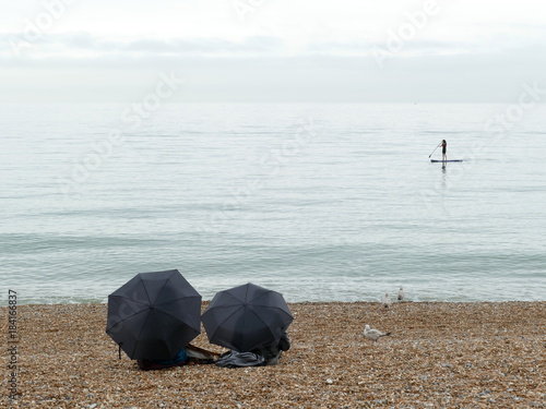 Paddle boarder on the sea with two umbrellas in foreground