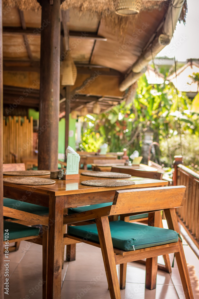 Fototapeta premium Interior of a tropical restaurant on Bali island, Indonesia. Wooden table and chairs.