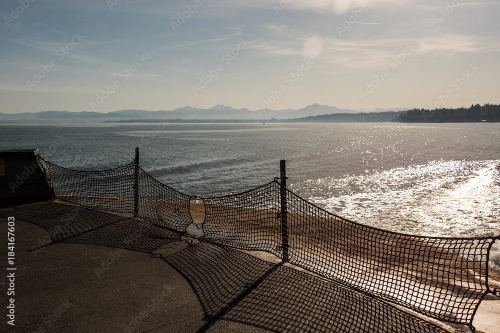 Sunrise over Puget Sound (water) and the Cascade Mountains with sun flare from a ferry deck