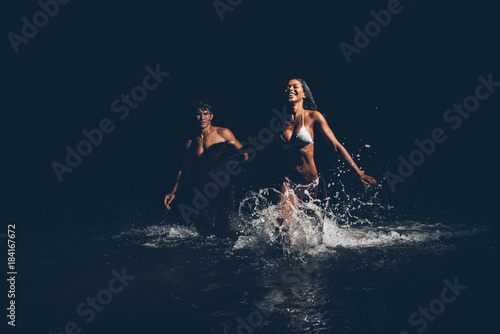 Young couple running in the ocean during the night bath