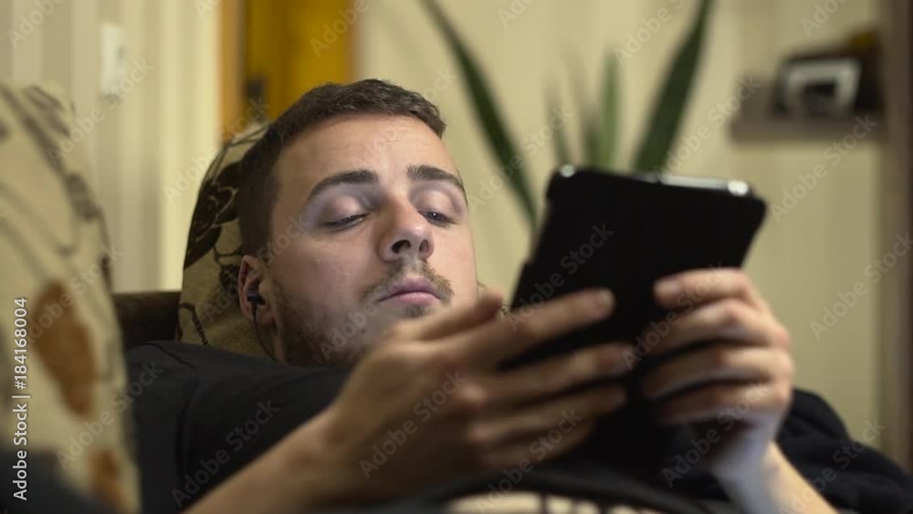 Medium shot of a man using a tablet on the bed and falling asleep Medium shot of a man using a tablet on the bed and falling asleep