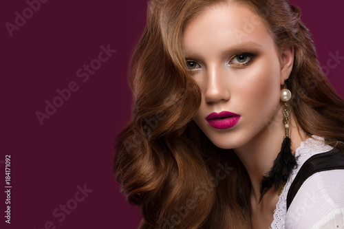 Beautiful redhair model  curls  bright makeup  jewelry and red lips. The beauty face. Portrait shot in the studio on a brown background.