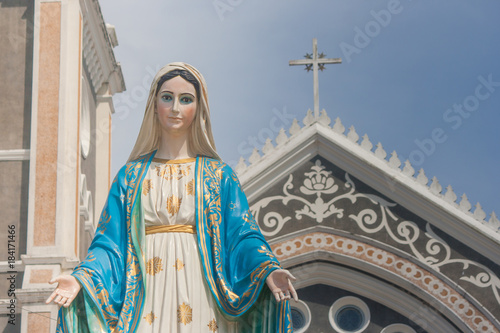 The Blessed Virgin Mary statue standing in front of The Cathedral of the Immaculate Conception at The Roman Catholic Diocese with crucifix and blue sky background at Chanthaburi Province, Thailand.