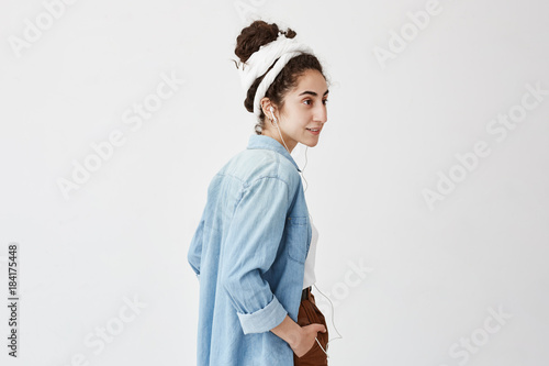 Fotografia Profile of female teenager listening to music or audio book while going to university, having happy expression, laughing, isolated against white background