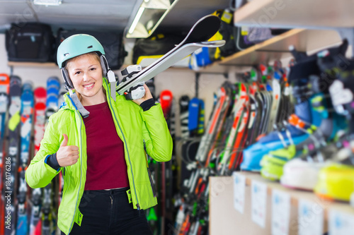 woman in jacket and helmet is demonstraiting ski in shop.
